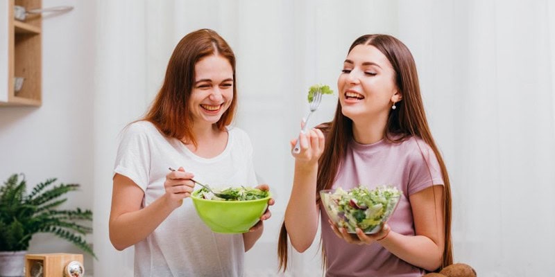 Two women enjoying fresh salads packed with brain-boosting foods that help reduce stress, balance mood, and improve sleep
